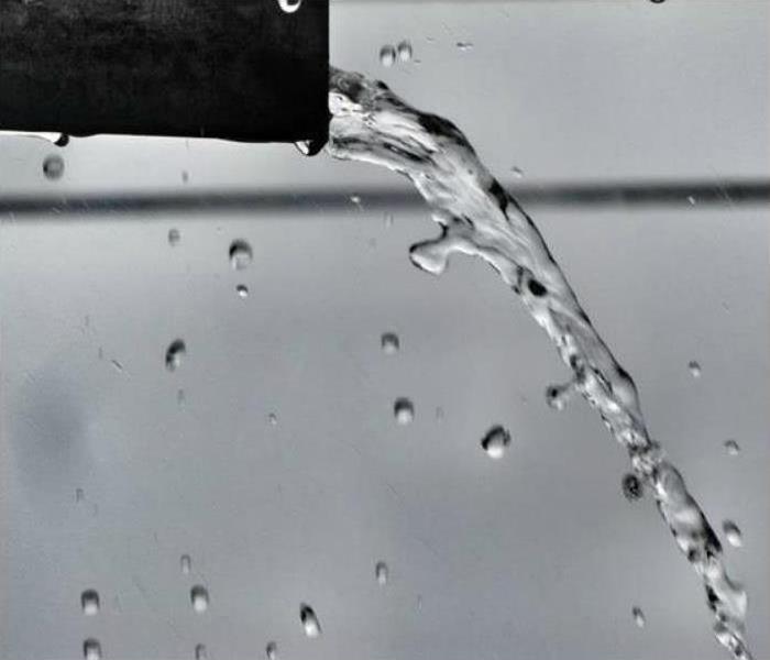 Water coming out of a black pipe with a grey background.